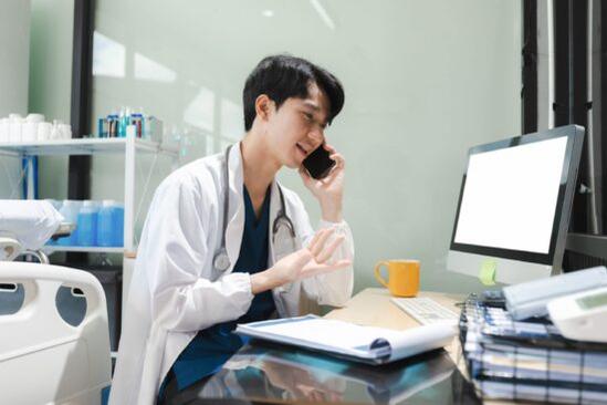 A physician speaking on the phone while sitting at his desk in a bright medical office.