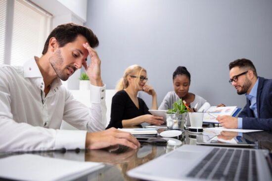 A man experiencing hidden mental health struggles and workplace stress during a group office meeting.